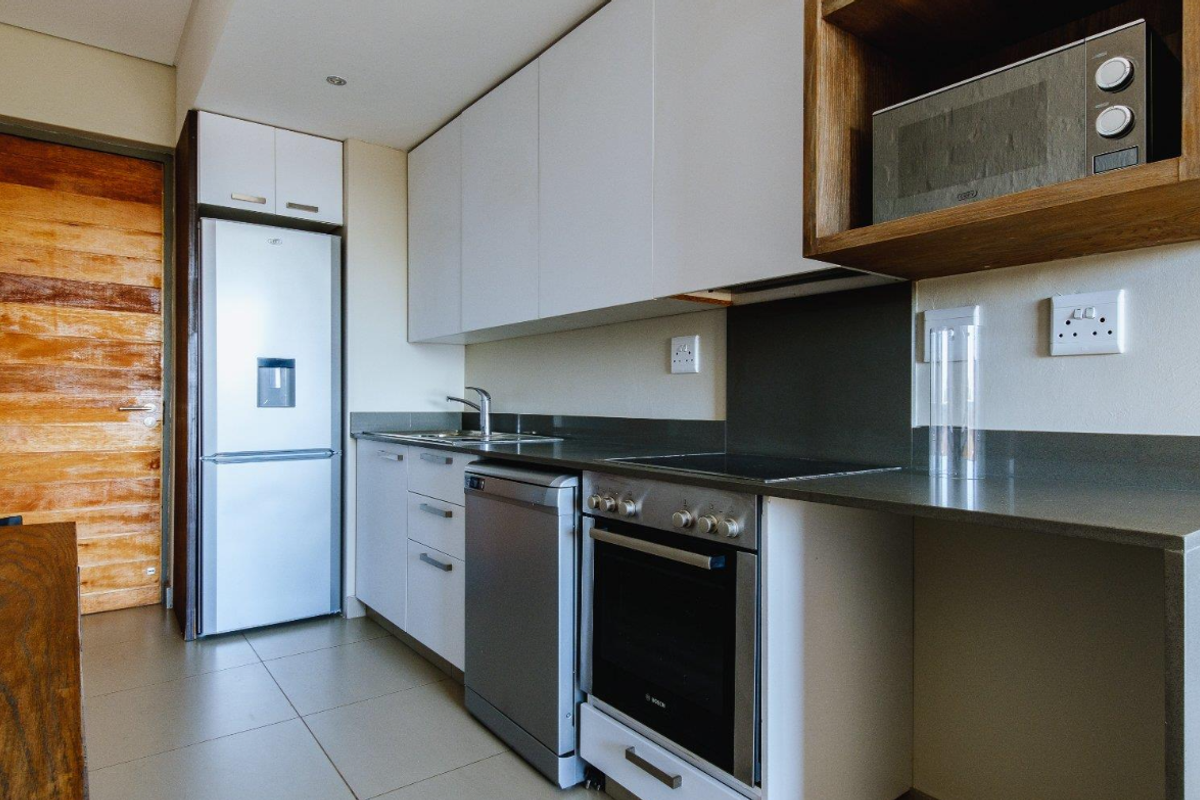 Modern kitchen featuring sleek white cabinetry, stone countertops, integrated oven and hob, and a dedicated space for a microwave.
