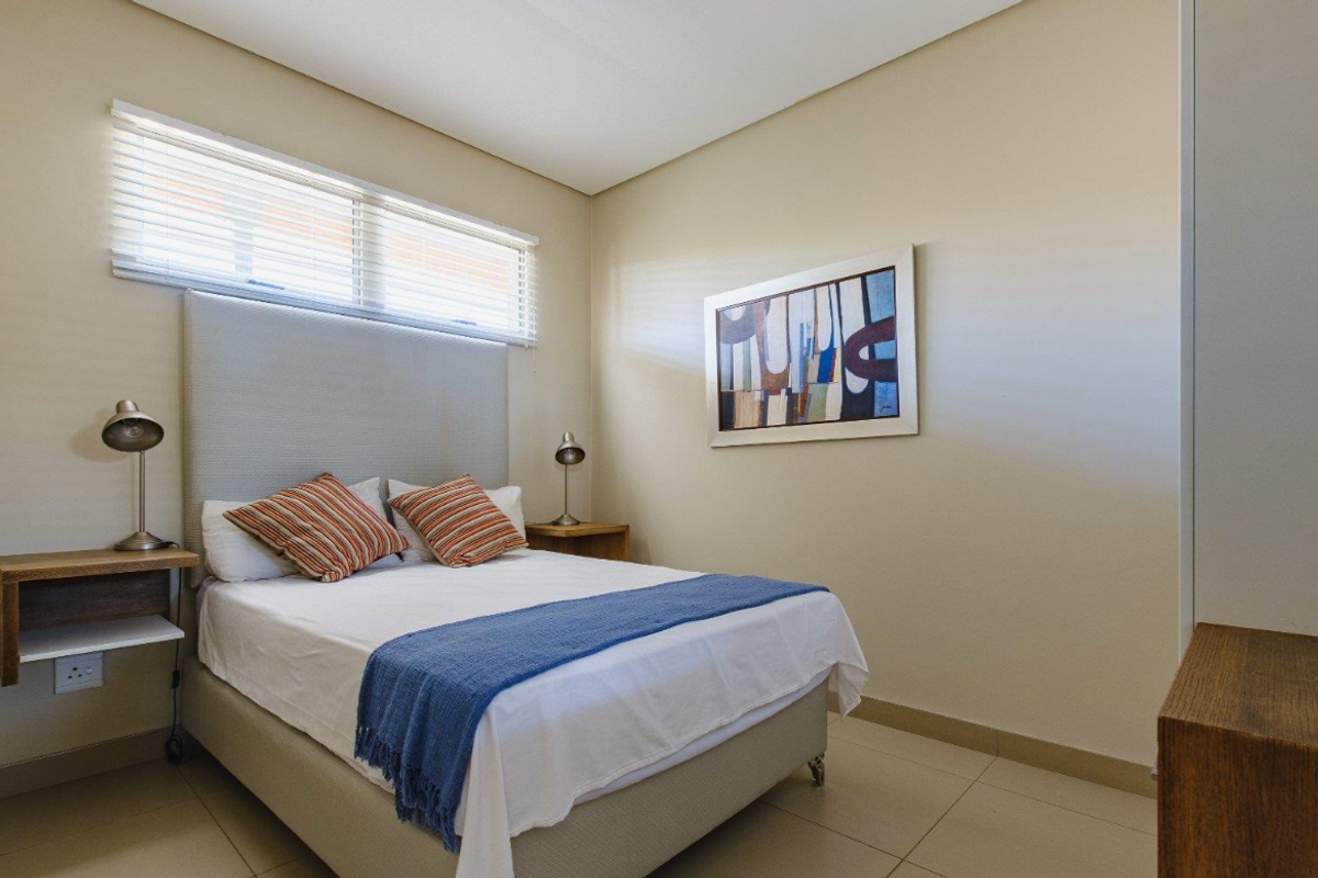 A well-maintained bedroom featuring neutral wall tones, tiled flooring, and a horizontal window with fitted blinds.