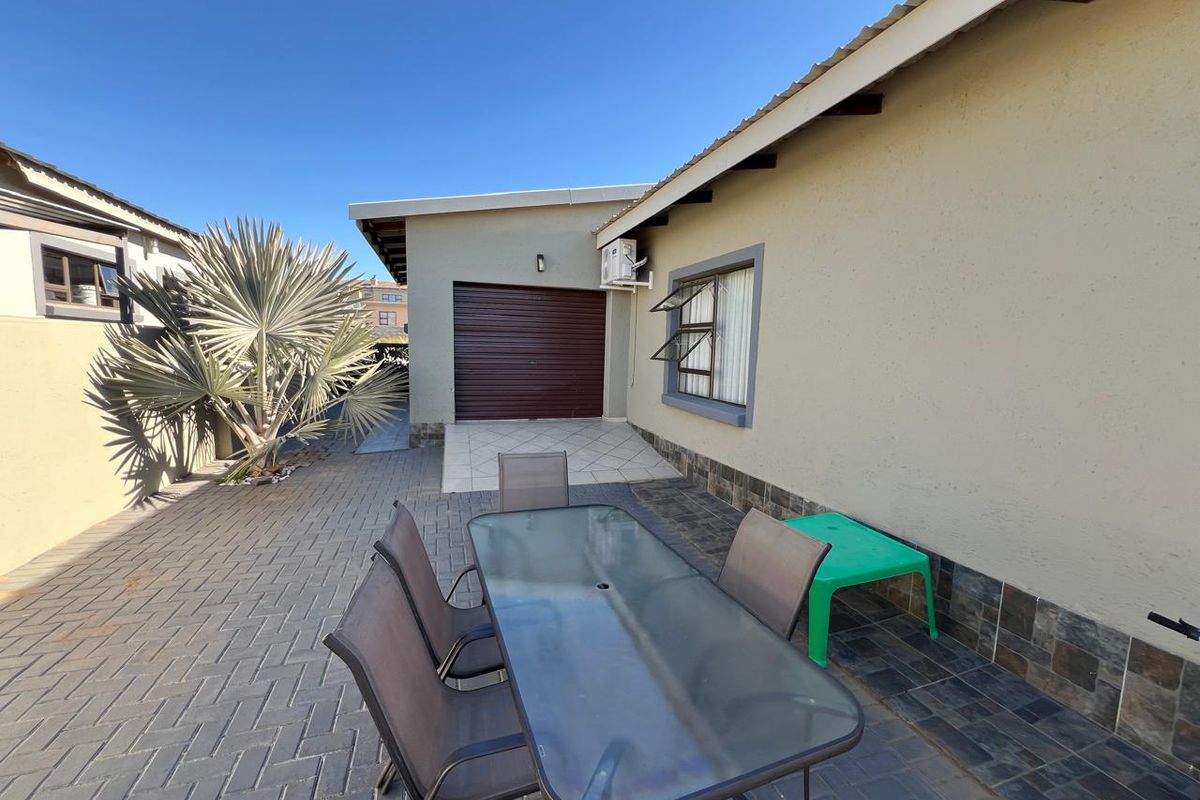 A paved rear patio area featuring a garage entrance, stone-clad wall accents, and a wall-mounted air conditioning unit.