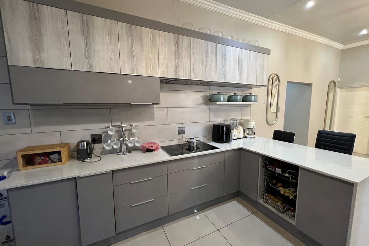 Modern kitchen featuring sleek grey and wood-grain cabinetry, stone countertops, integrated induction cooktop, and contemporary tiled backsplash with large-format floor tiles.