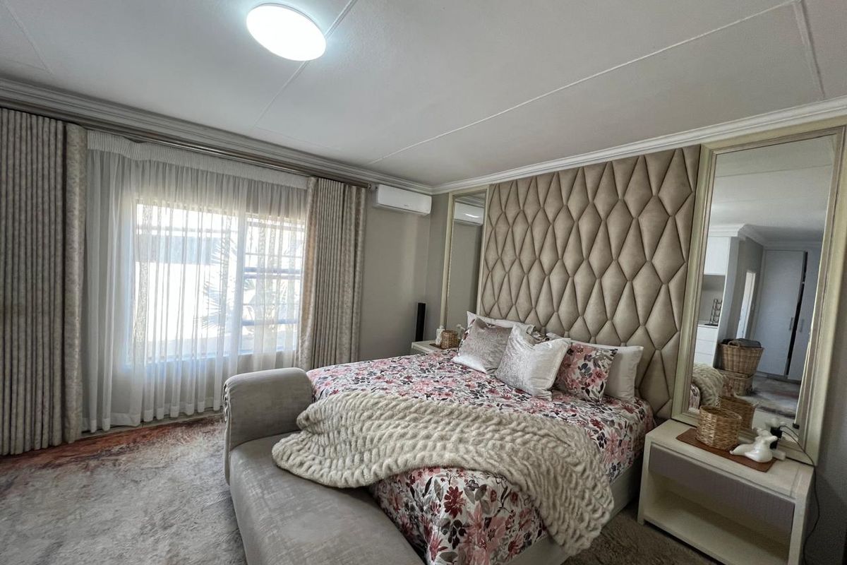 A well-maintained bedroom featuring a large upholstered feature headboard, integrated mirrored panels, and a wall-mounted air conditioning unit.