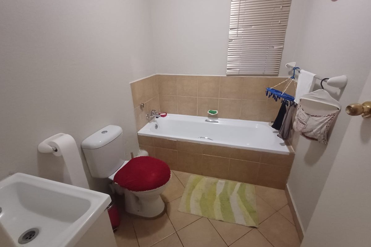 A functional bathroom featuring a built-in bathtub with tiled surround, a standard toilet, and a pedestal basin with tiled flooring.