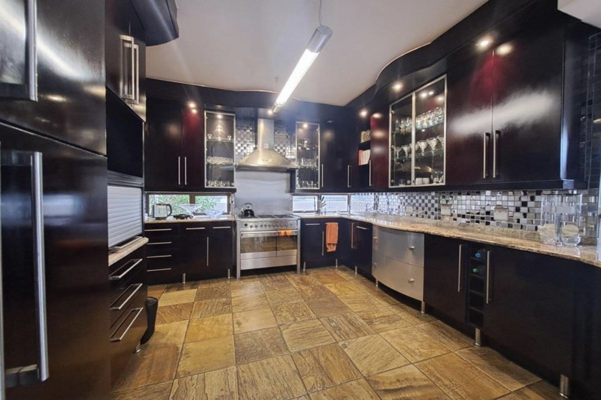 A spacious kitchen featuring dark cabinetry, granite countertops, a stainless steel gas range with extractor fan, and tiled flooring.
