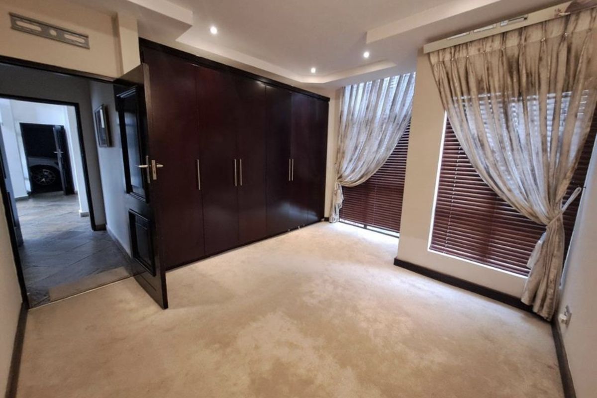 A well-maintained bedroom featuring built-in dark wood cabinetry, recessed ceiling lighting, and large windows with fitted blinds and curtains.
