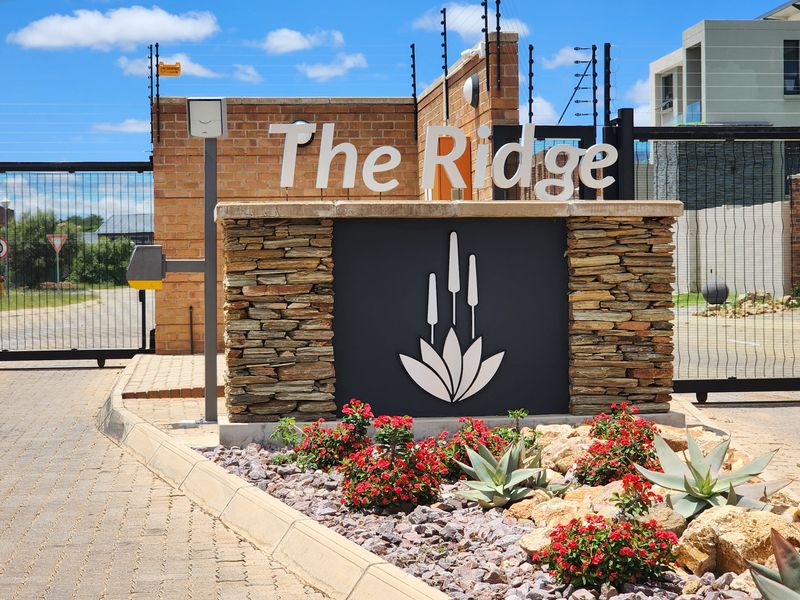 The entrance to The Ridge estate, featuring a stone-clad signage wall, electric fencing, and secure gated access with paved driveway.