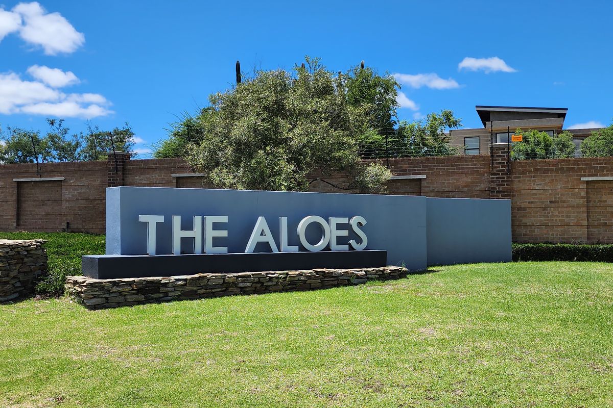 Entrance signage for The Aloes residential estate, featuring a modern stone and concrete monument set within a well-maintained landscaped garden.