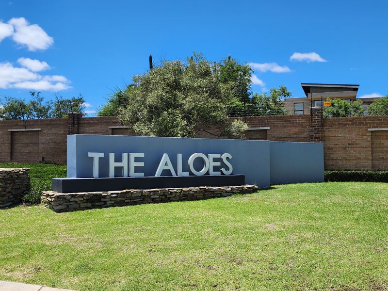 Entrance signage for The Aloes residential estate, featuring a modern stone and concrete monument set within a well-maintained landscaped garden.