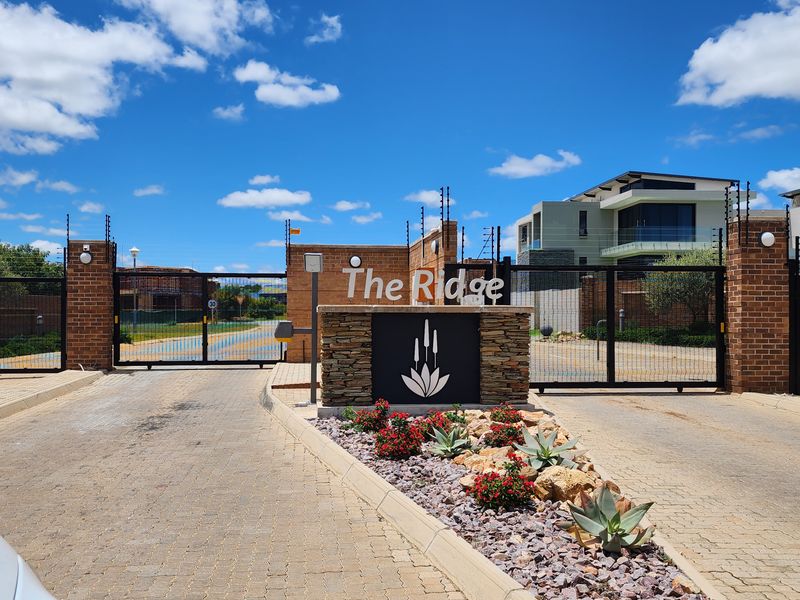 The secure gated entrance to The Ridge residential estate, featuring brick pillars, electric fencing, and landscaped garden beds.