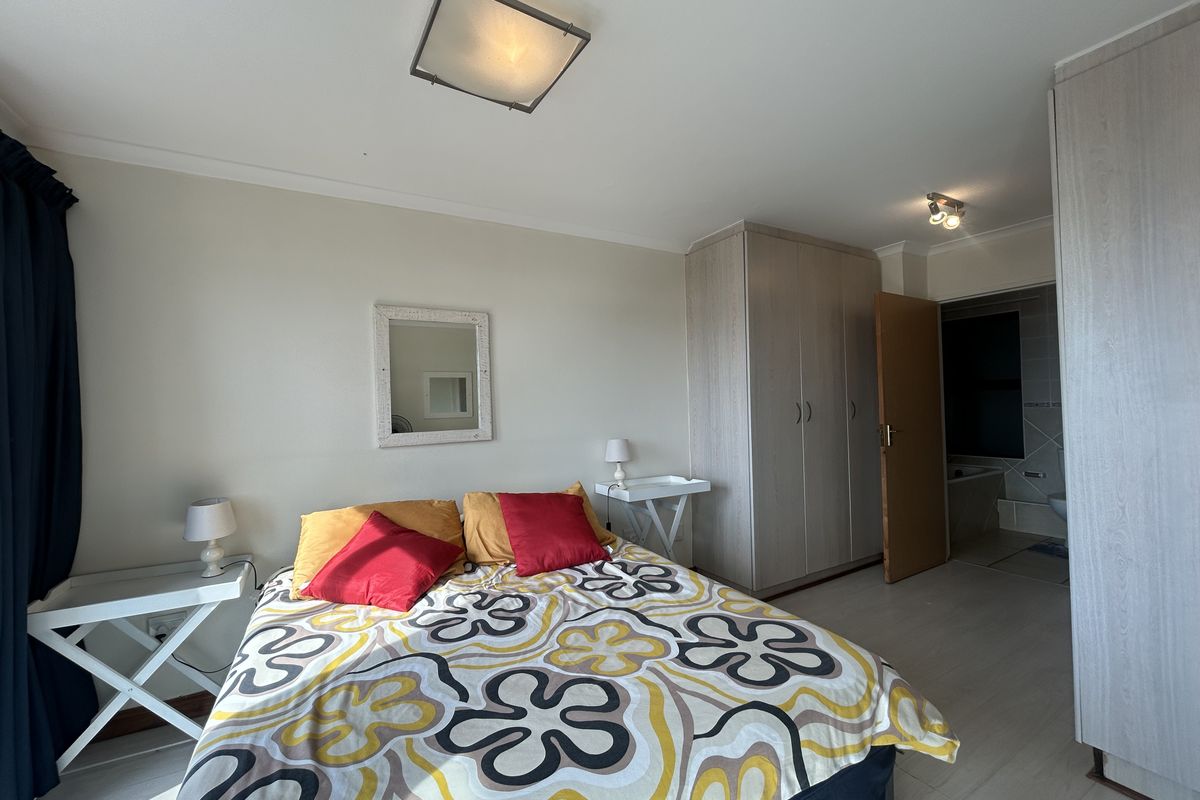 A bedroom featuring built-in wardrobes, light-toned flooring, and an en-suite bathroom access.