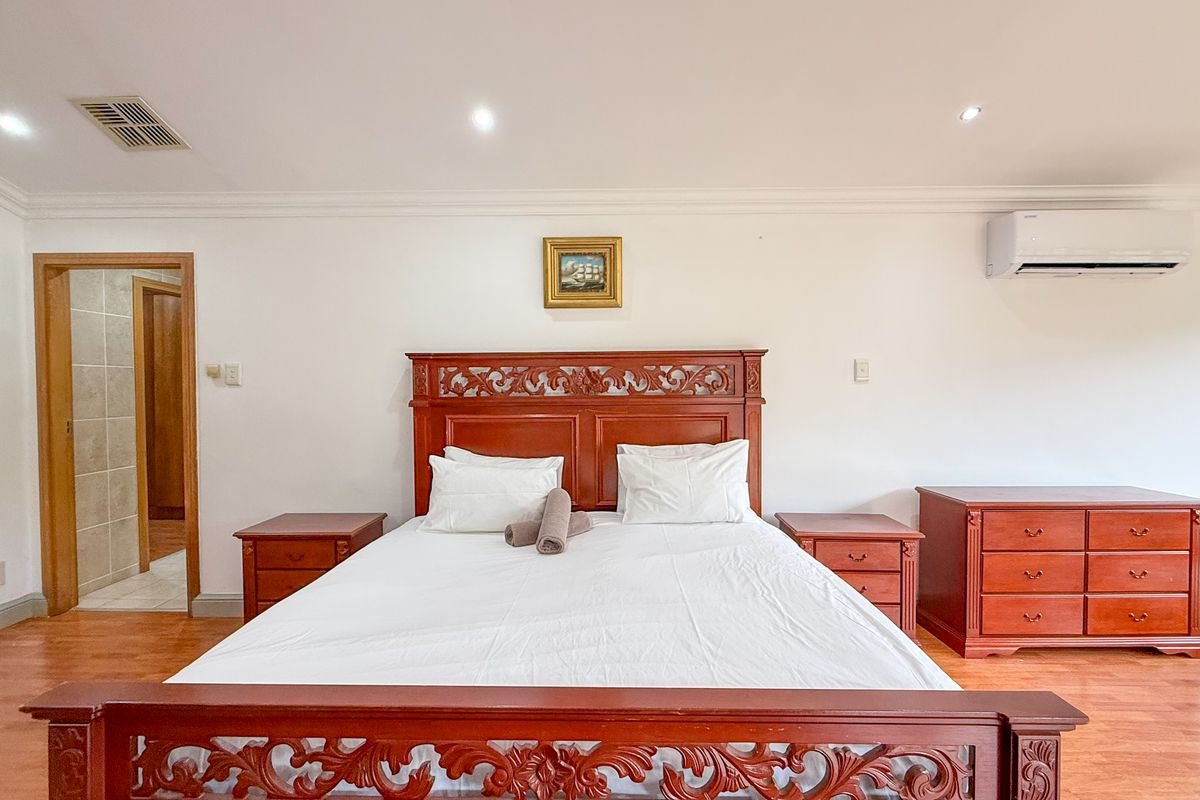 A well-maintained bedroom featuring laminate flooring, recessed downlighting, and a wall-mounted air conditioning unit.