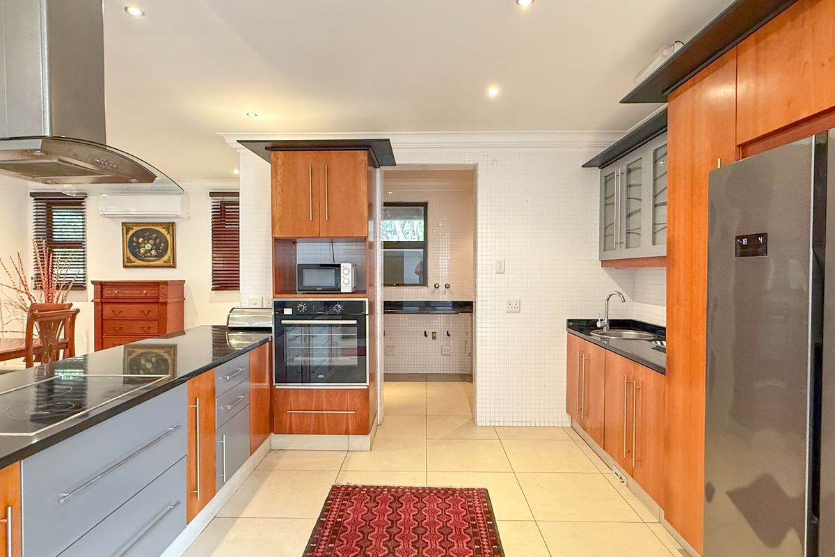 Modern kitchen featuring wood-toned cabinetry, stone countertops, built-in oven, extractor fan, and a tiled splashback, with an adjacent scullery area.