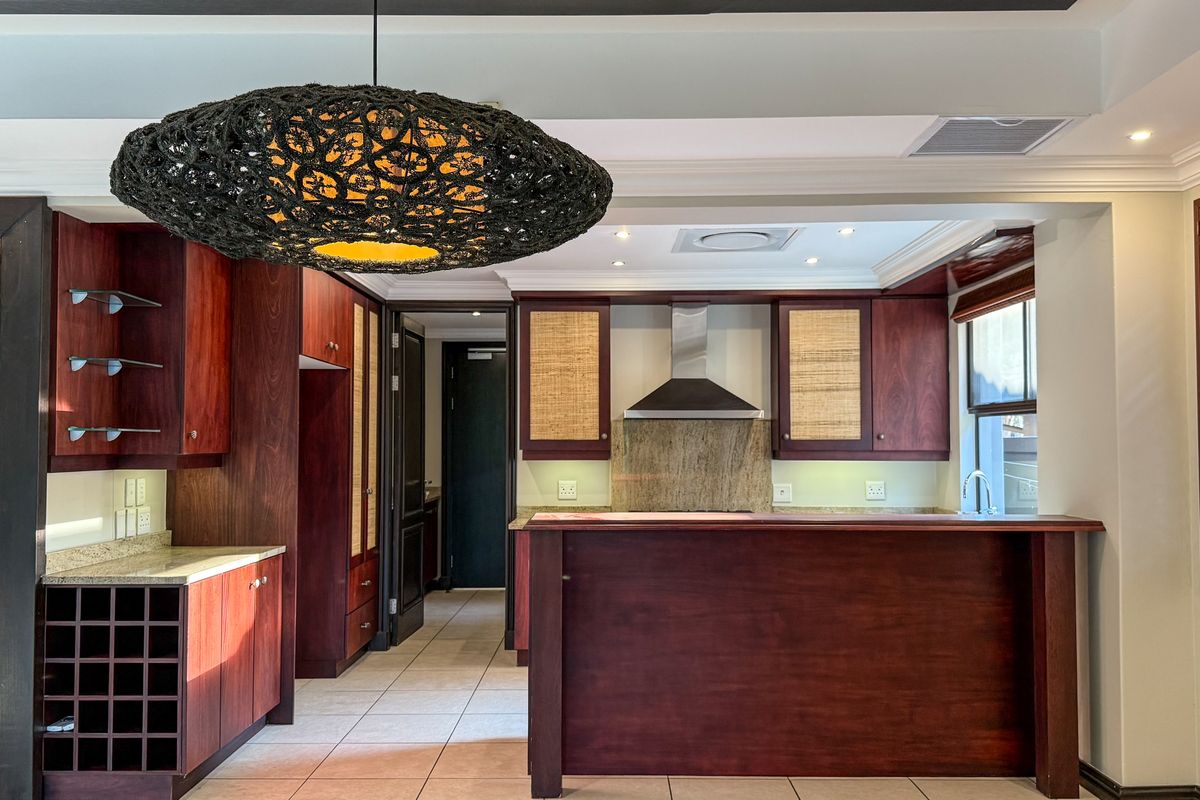 A well-appointed kitchen featuring rich wood cabinetry, stone countertops, a built-in extractor fan, and a dedicated wine rack, complemented by elegant plantation shutters.