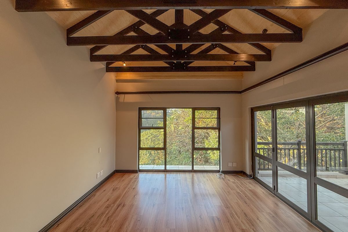 Spacious living area featuring high vaulted ceilings with exposed timber trusses, laminate flooring, and large windows providing abundant natural light and garden views.