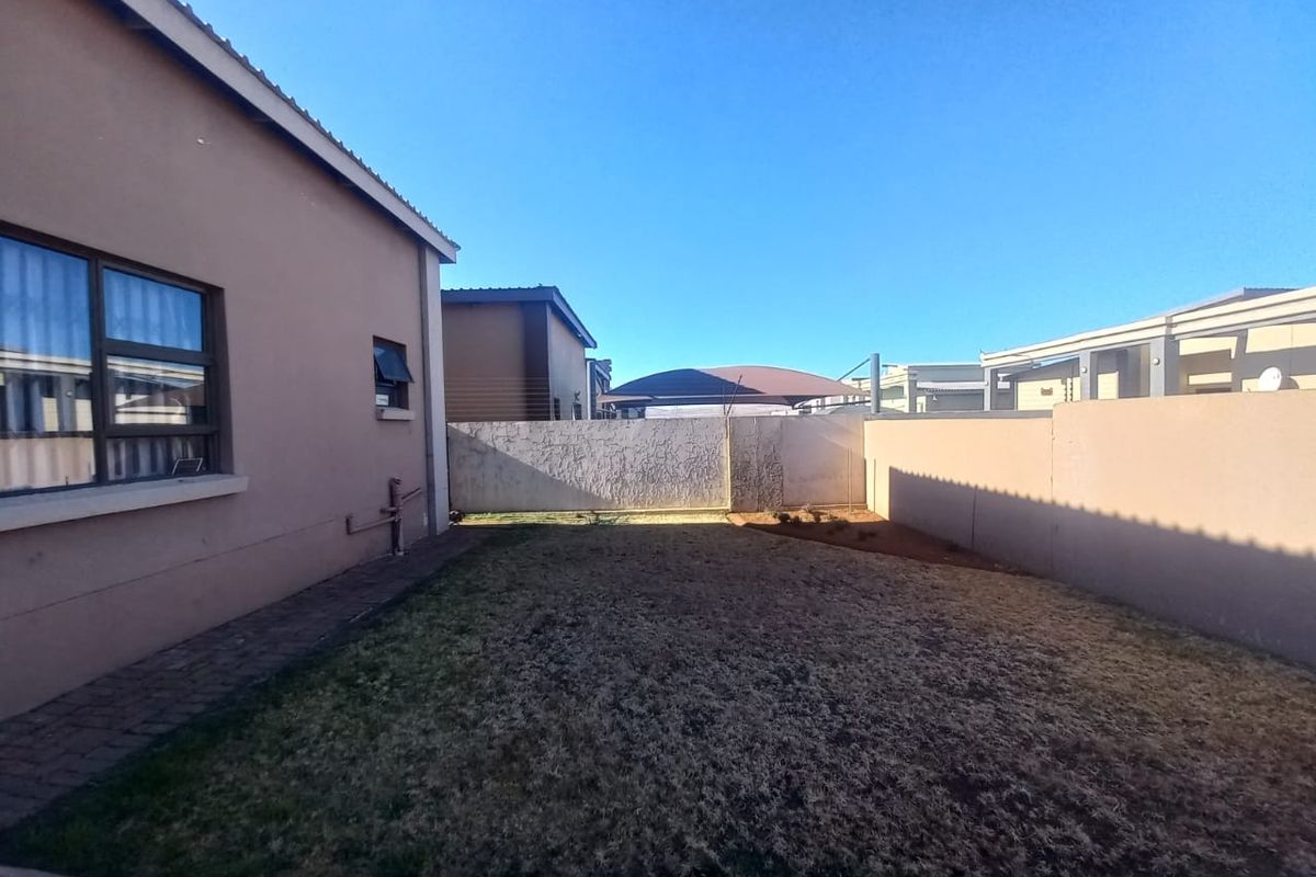 A private rear garden area featuring a lawn, paved walkway, and high perimeter boundary walls for added privacy.