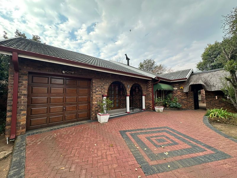 Front exterior view of a brick house featuring a paved driveway, integrated garage, and a combination of tiled and thatched roofing.