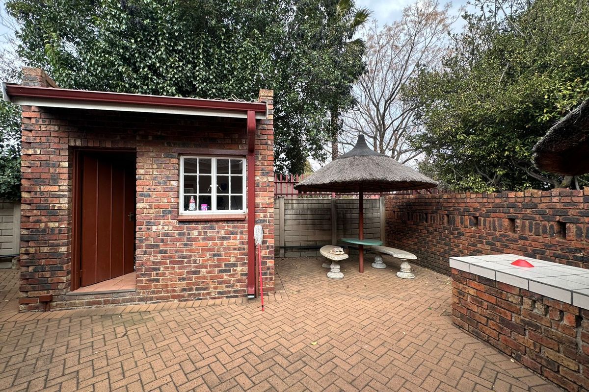 Rear courtyard featuring brick paving, a built-in brick braai, and a thatched outdoor seating area adjacent to a brick outbuilding.