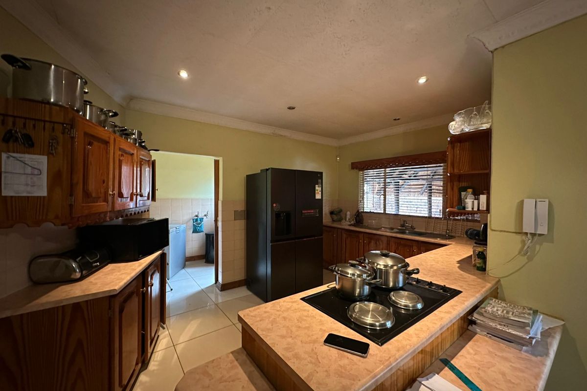 A functional kitchen featuring wooden cabinetry, laminate countertops, an integrated electric hob, and tiled flooring, with an adjacent scullery area.
