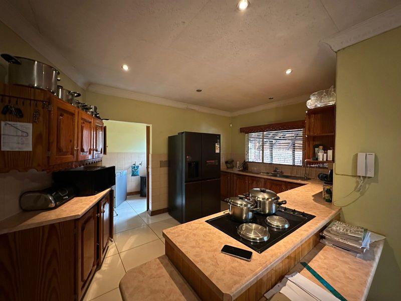 A functional kitchen featuring wooden cabinetry, laminate countertops, an integrated electric hob, and tiled flooring, with an adjacent scullery area.