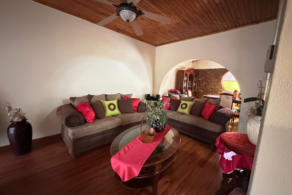 Living room featuring a timber ceiling with a fan, laminate flooring, and an arched opening leading to an adjacent space with exposed brickwork.