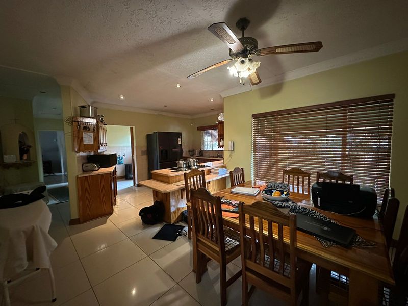 Open-plan kitchen and dining area featuring tiled flooring, a central kitchen island with a cooktop, and wooden blinds.