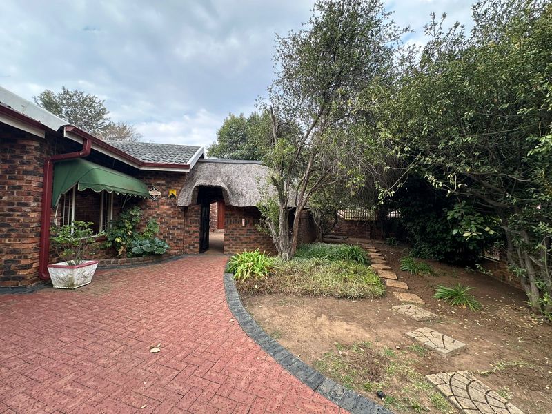Front entrance area featuring a brick facade, a unique thatched roof section, and a paved driveway leading to the main entry.