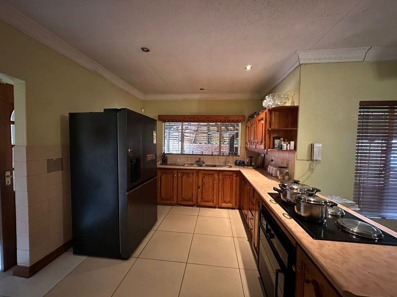 A functional kitchen featuring wooden cabinetry, laminate countertops, built-in oven, electric hob, and tiled flooring with recessed lighting.