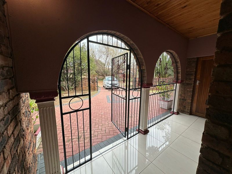 A covered patio area featuring arched wrought iron security gates, tiled flooring, and a timber ceiling, overlooking a paved driveway.