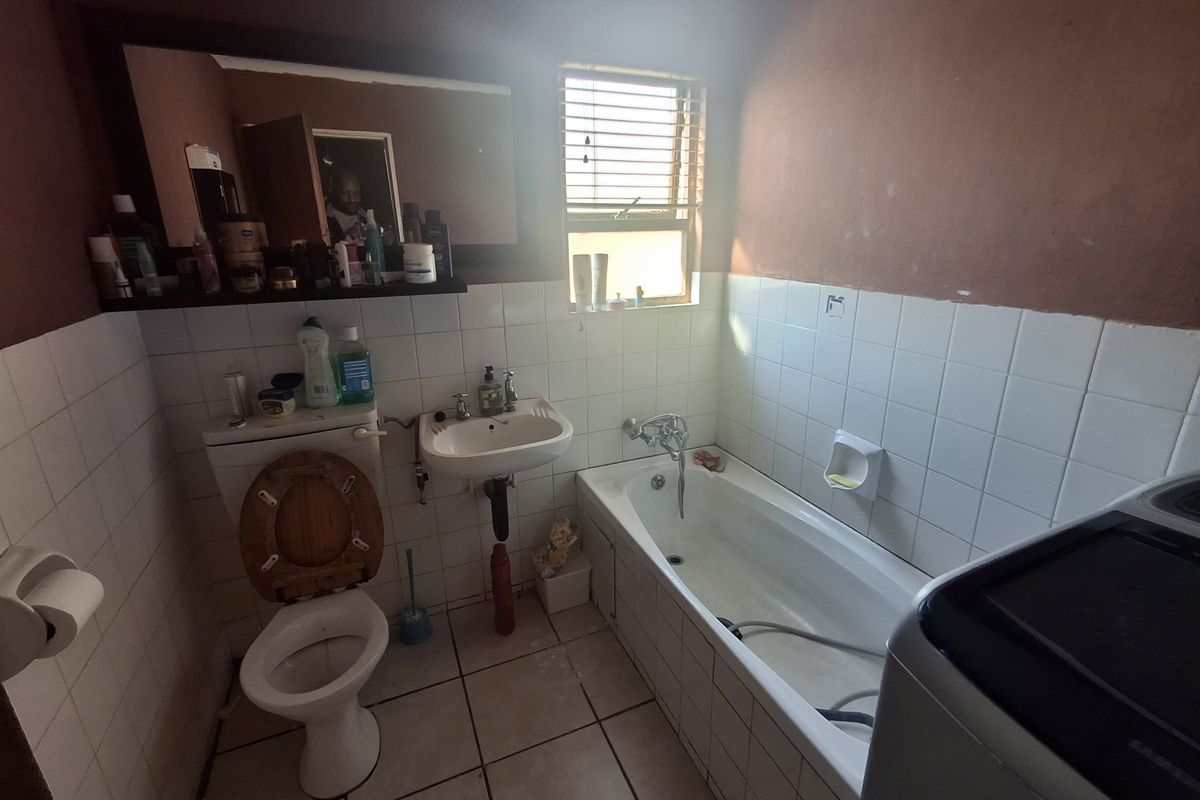 A functional bathroom featuring a standard bathtub, wall-mounted basin, and toilet, with tiled walls and flooring.