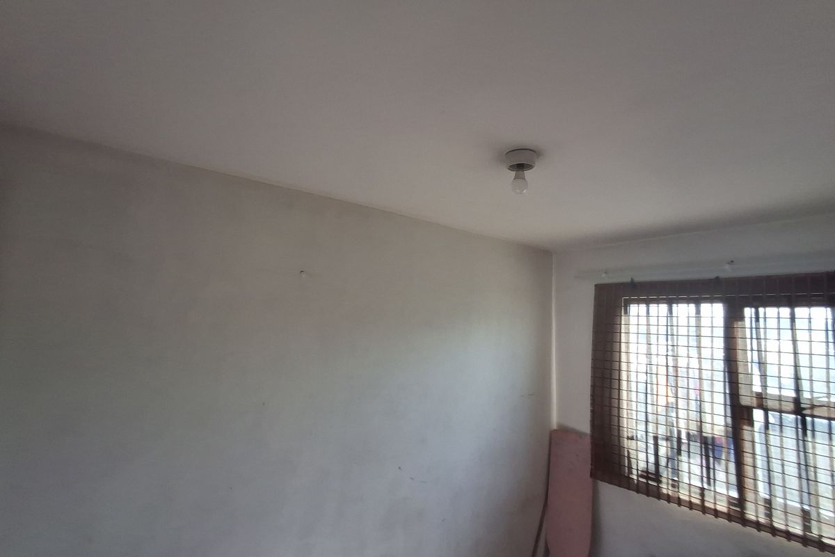 A simple bedroom featuring a window with security bars and a basic ceiling light fixture, offering a blank canvas for potential updates.