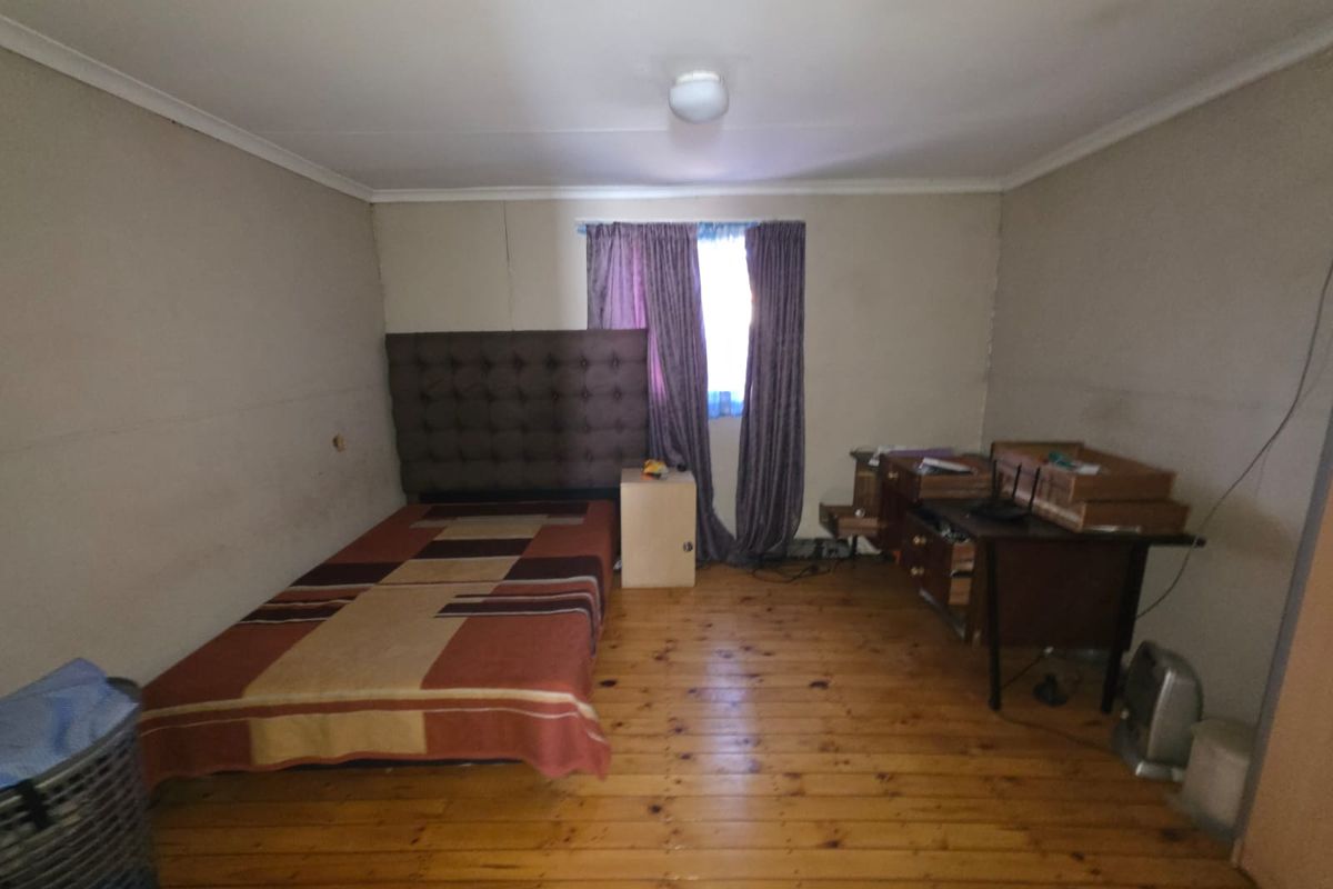 A bedroom featuring timber flooring and a window with curtains, providing a functional space with potential for cosmetic updates.