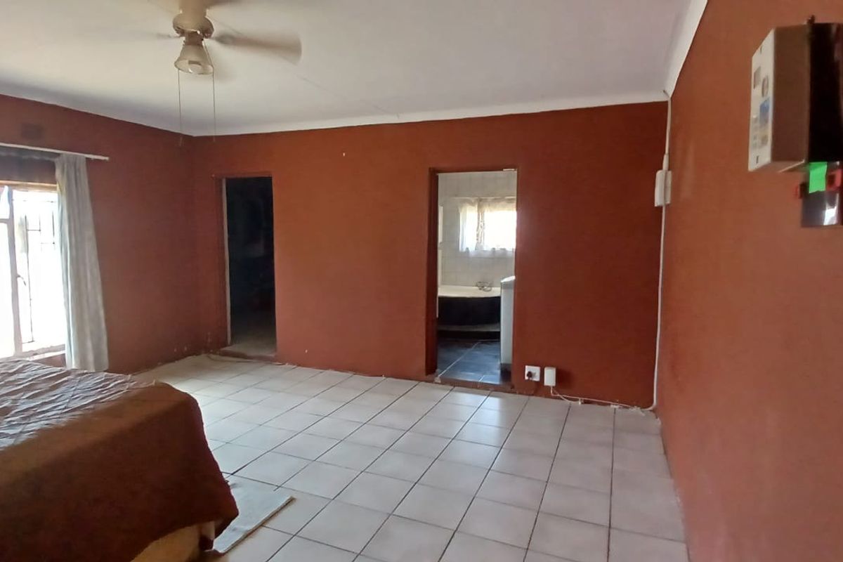 A spacious bedroom featuring tiled flooring, a ceiling fan, and direct access to an en-suite bathroom.