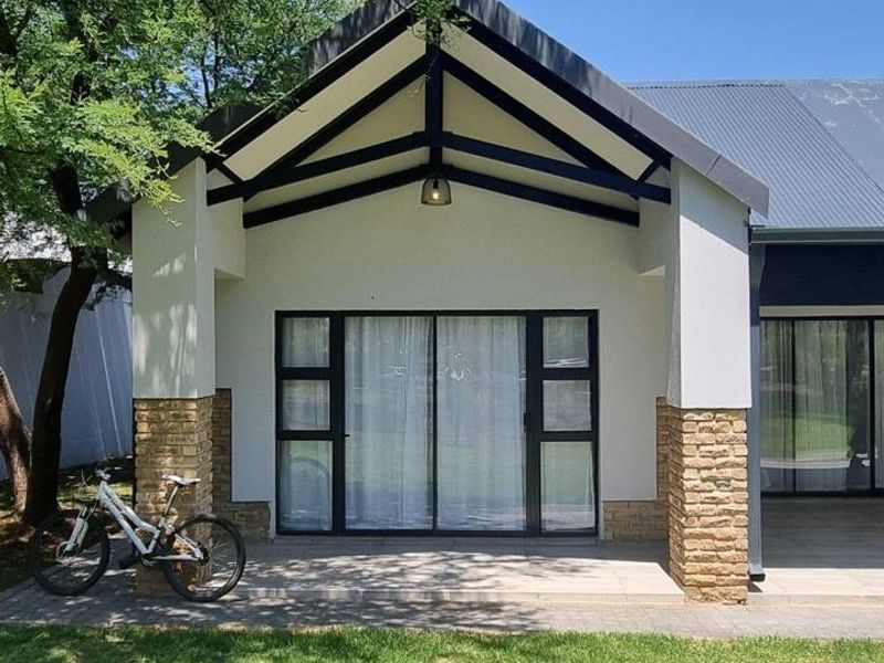 A well-maintained covered patio featuring stone-clad pillars, exposed timber roof trusses, and large sliding glass doors leading into the home.