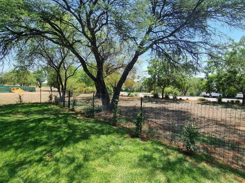 A spacious garden area featuring a well-maintained lawn, mature trees, and perimeter wire mesh fencing.