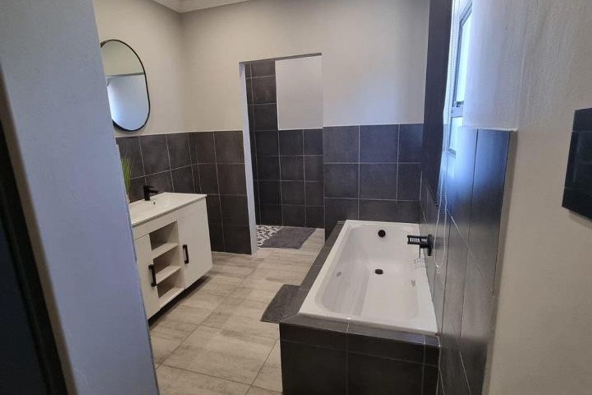 Modern bathroom featuring a built-in vanity, bathtub, and a separate walk-in shower area with contemporary dark wall tiles and light floor tiles.