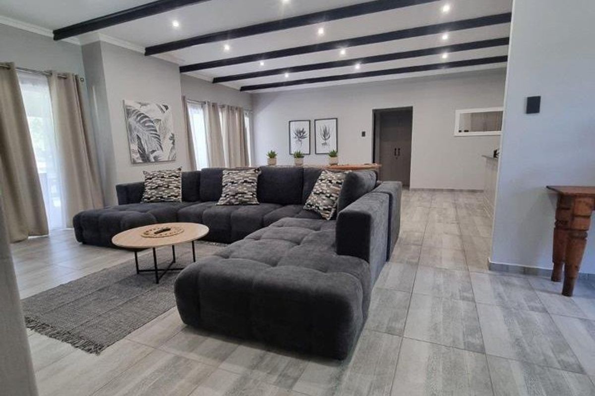 Spacious living area featuring modern tiled flooring, exposed ceiling beams, and recessed downlighting, creating a bright and contemporary open-plan atmosphere.