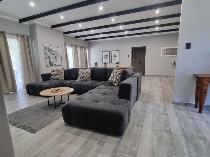 Spacious living area featuring modern tiled flooring, exposed ceiling beams, and recessed downlighting, creating a bright and contemporary open-plan atmosphere.