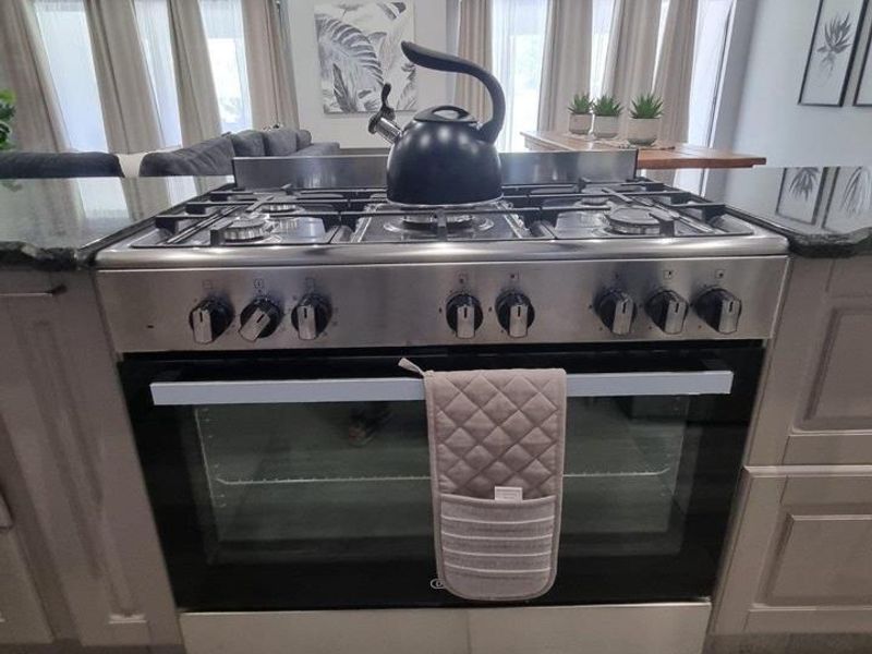 A modern kitchen featuring a stainless steel gas stove, granite countertops, and classic shaker-style cabinetry, set against a neutral tiled floor.