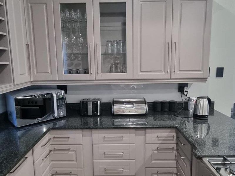 A well-maintained kitchen featuring granite countertops, ample built-in cabinetry with glass-front display sections, and integrated appliances including a microwave and gas cooktop.