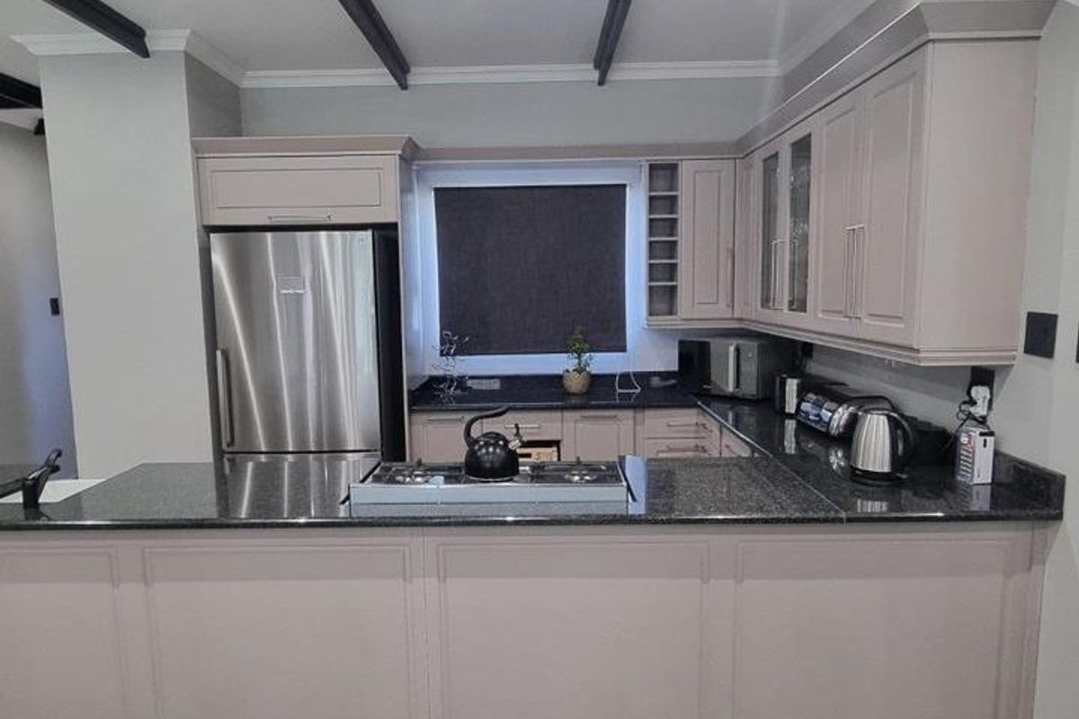 Modern kitchen featuring neutral cabinetry, granite countertops, a gas hob, and decorative ceiling beams, offering a clean and functional culinary space.
