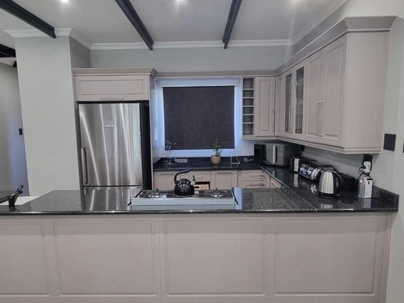 Modern kitchen featuring neutral cabinetry, granite countertops, a gas hob, and decorative ceiling beams, offering a clean and functional culinary space.