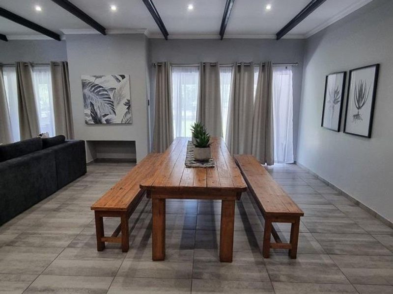 Spacious dining area featuring modern tiled flooring, exposed ceiling beams, and large windows that provide ample natural light.