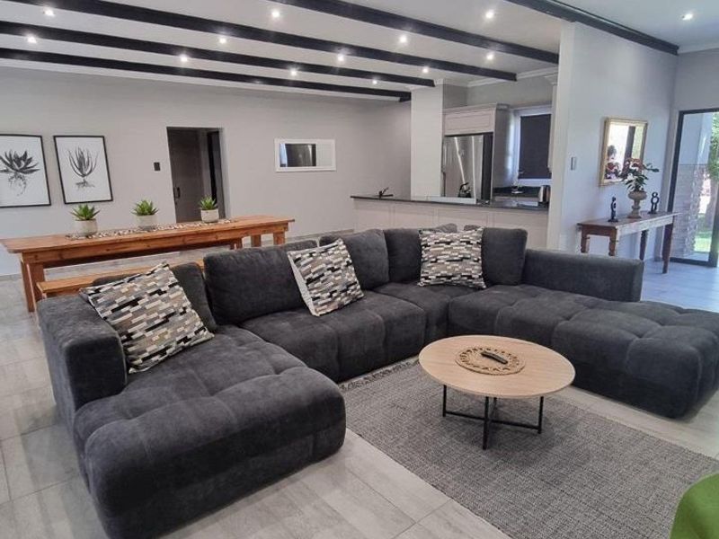 Spacious open-plan living area featuring modern tiled floors, striking exposed ceiling beams, recessed lighting, and a seamless transition to the kitchen space.