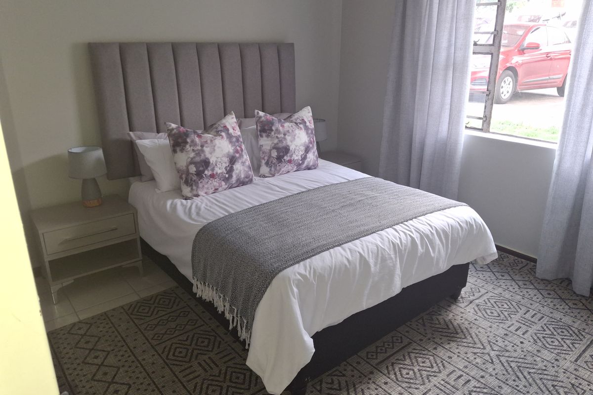 A well-lit bedroom featuring neutral wall tones, tiled flooring, and a large window allowing for natural light.