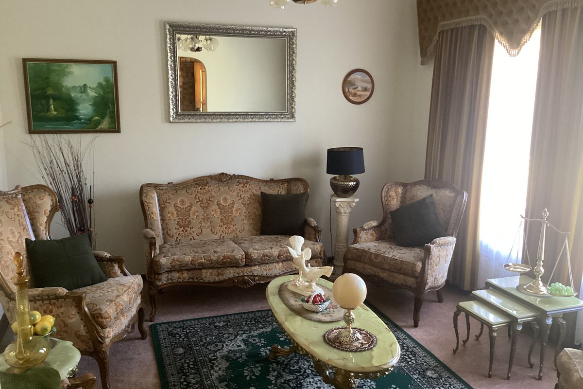 A traditional living room featuring carpeted flooring, a large window with decorative pelmet and curtains, and a central ceiling light fixture.
