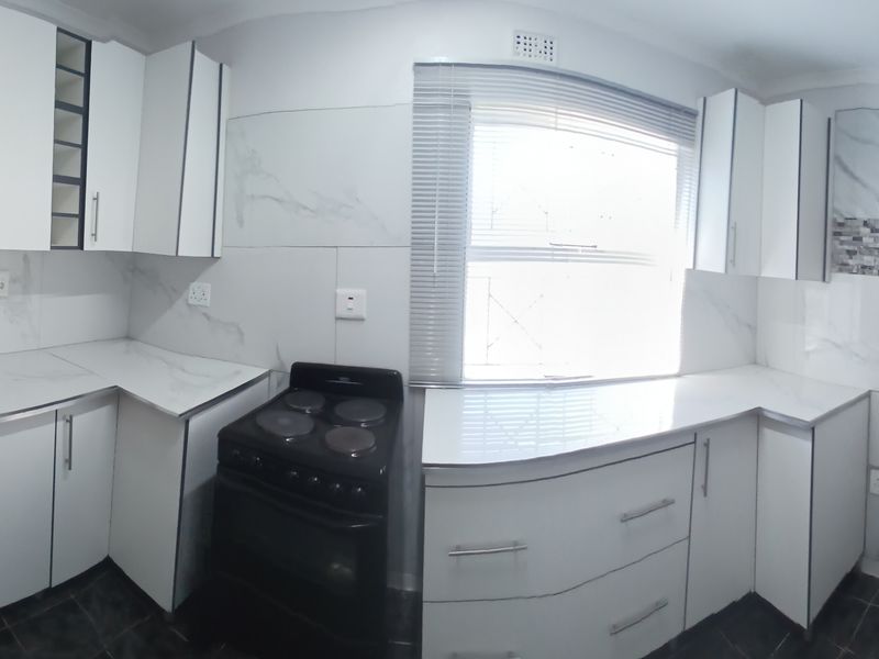 A modern, clean kitchen featuring white cabinetry, marble-look countertops, a double basin sink, and an electric stove with a tiled backsplash.