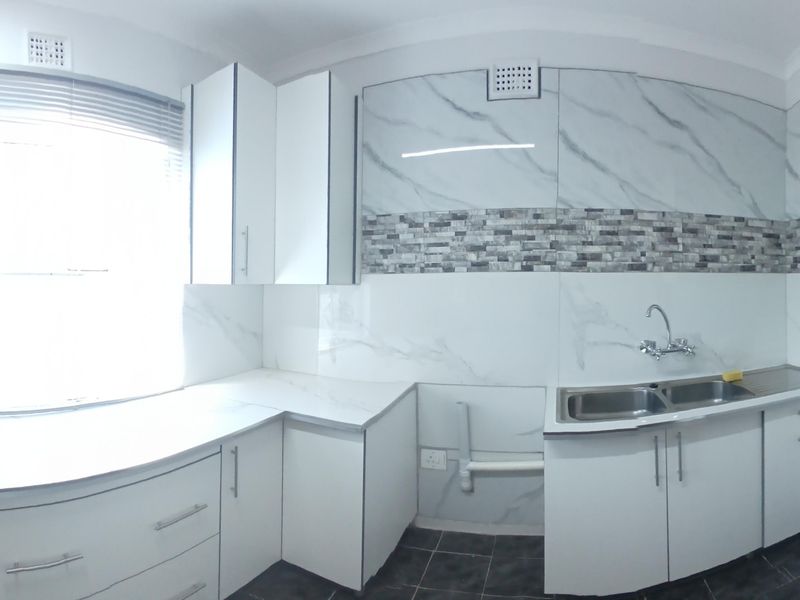 A bright, modern kitchen featuring white cabinetry, marble-look splashbacks, a double bowl sink, and an electric stove, presented in a clean, empty space.