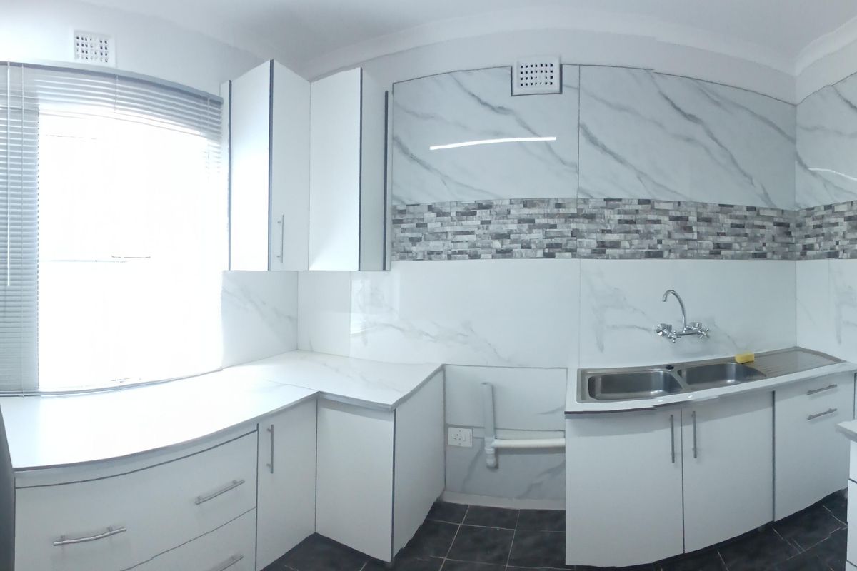 A bright, modern kitchen featuring white cabinetry, marble-look splashbacks, a double bowl sink, and an electric stove, presented in a clean, empty space.