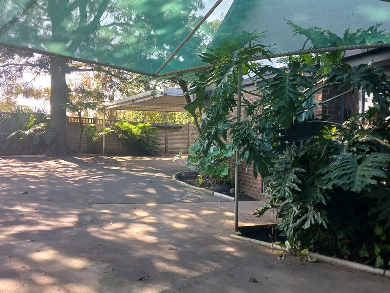 A paved rear outdoor area featuring a shade sail structure, brick walling, and established garden greenery.