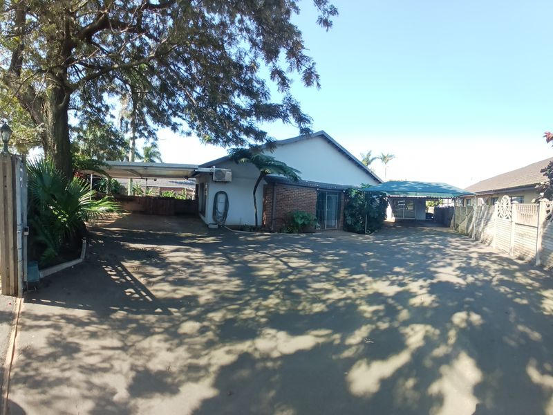 Spacious front exterior featuring a large paved driveway, covered carport parking, and established trees, providing ample off-street parking space.