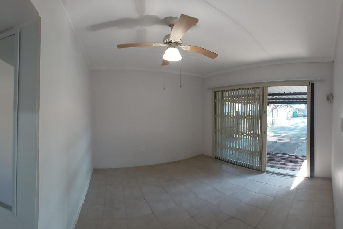 An empty living room featuring tiled flooring, a ceiling fan, and a sliding glass door with a security gate leading to the exterior.